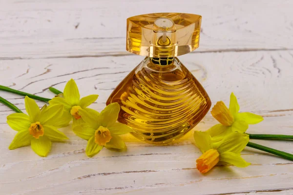 Women perfume with yellow daffodil flowers on white wooden background