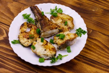 Ahşap bir masada beyaz tabakta kavrulmuş pollock.