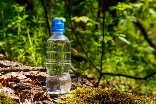 Plastikowa butelka ze słodką wodą pitną na zielonym tle lasu — Zdjęcie stockowe