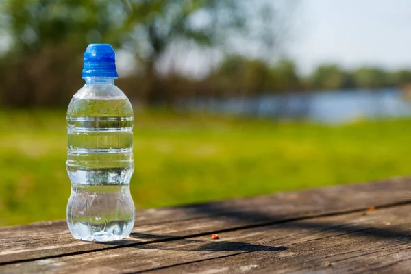 Plastikowa butelka ze świeżą wodą pitną na drewnianym stole na tle natury — Zdjęcie stockowe