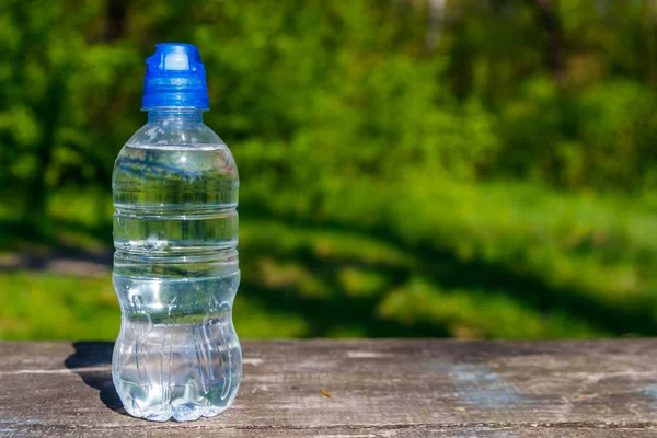 Botella de plástico con agua potable fresca sobre una mesa de madera sobre fondo natural — Foto de Stock