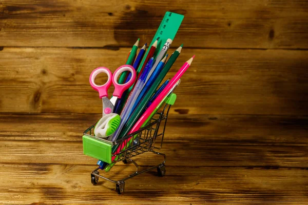 Comprando útiles escolares. Carro de compras con útiles escolares sobre un fondo de madera. Regreso al concepto escolar —  Fotos de Stock