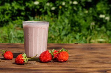 Dışarıdaki ahşap masada bir bardak taze çilekli smoothie. 
