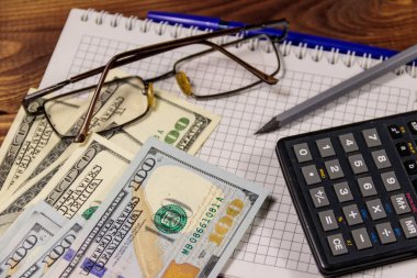 Defter ile dolar, kalem, gözlük ve ahşap masa hesap makinesi. Mali kavramı. İş rapor