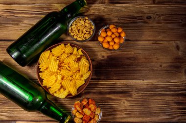 Bira şişeleri ve ahşap masada bira için çeşitli atıştırmalıklar.