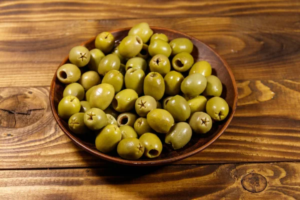 Plaat met groene olijven op houten tafel — Stockfoto