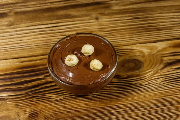 Tigela de vidro com deliciosa avelã de chocolate espalhada na mesa de madeira — Fotografia de Stock