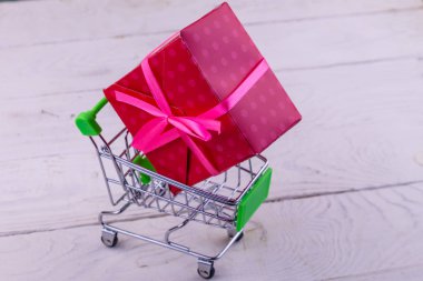 Beyaz ahşap arka plan üzerinde büyük hediye kutusu ile Alışveriş sepeti