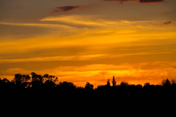 Pôr-do-sol laranja sobre silhuetas de aldeia e árvores — Fotografia de Stock