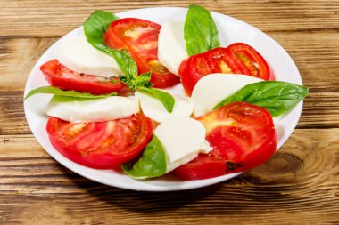 Domatesli İtalyan caprese salatası, ahşap bir masada mozzarella peyniri ve fesleğen.
