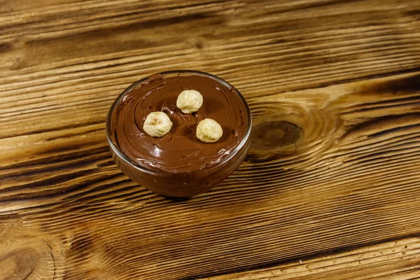 Ciotola di vetro con deliziosa nocciola al cioccolato spalmata su tavolo di legno — Foto Stock