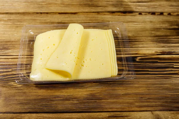 Tek kullanımlık plastik bir kutuda dilimler halinde peynir, ahşap bir masada. — Stok fotoğraf