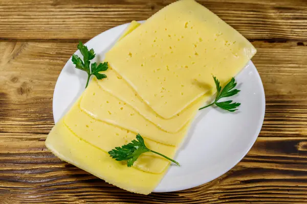 Rebanadas de queso en un plato sobre una mesa de madera. Vista superior —  Fotos de Stock