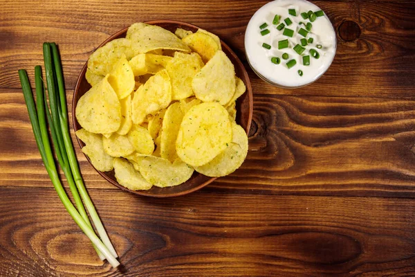 Хрусткі картопляні чіпси з зеленою цибулею та сметаною на дерев'яному столі. Вид зверху — стокове фото