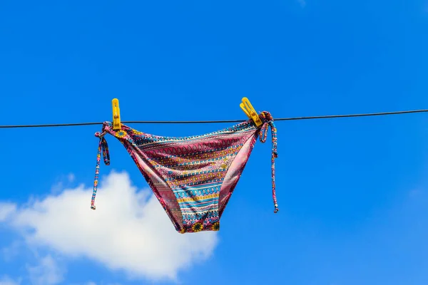 Traje de baño femenino de secado colgado de una cuerda contra el cielo azul — Foto de Stock