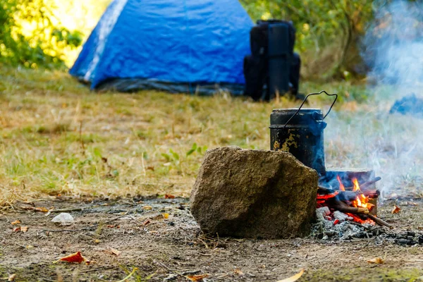 Cooking on campfire in camping. Tent and backpack on background