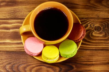 Bir fincan kahve ile lezzetli renkli macarons ahşap masa üzerinde. Üstten görünüm