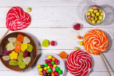 Renkli çikolatalı şekerler, lolipoplar ve jöleli şekerler beyaz ahşap masada.