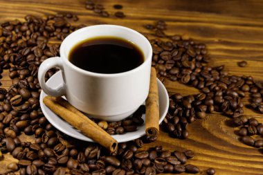 Bir fincan kahve, kavrulmuş kahve çekirdekleri ve ahşap masada tarçın çubukları.