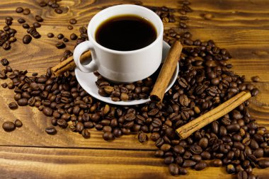 Bir fincan kahve, kavrulmuş kahve çekirdekleri ve ahşap masada tarçın çubukları.