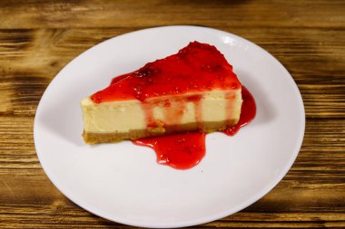Ahşap masa üzerinde beyaz bir tabak içinde ahududu reçeli ile lezzetli New York cheesecake parçası