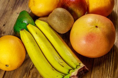 Ahşap masa üzerinde tropikal meyve çeşitleri. Muz, mango, portakal, avokado, greyfurt ve kivi ile natürmort