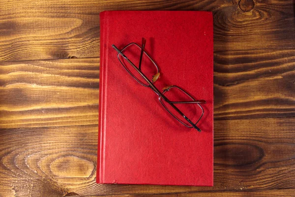 Closed book and eyeglasses on wooden background