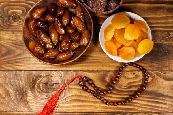 Dried apricots and dates fruit with wooden rosary on wooden table. Top view. The Muslim feast of the holy month of Ramadan