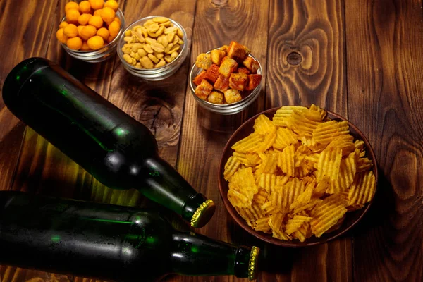 Bottles of beer and various snacks for beer on wooden table