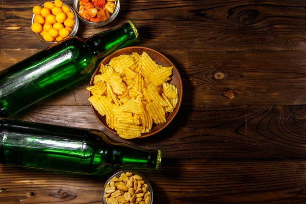 Bottles of beer and various snacks for beer on wooden table. Top view, copy space