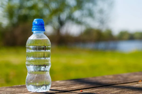 Plastikowa Butelka Świeżą Wodą Pitną Drewnianym Stole Tle Natury — Zdjęcie stockowe