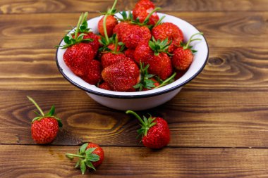 Tahta bir masada beyaz kasede taze olgun çilek.