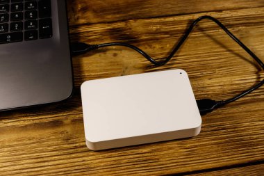 Harici HDD, tahta bir masadaki dizüstü bilgisayara bağlı. Veri depolama kavramı