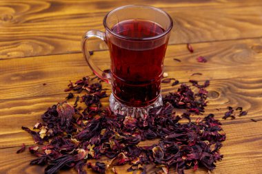 Ahşap masada bir bardak kırmızı amber çayı (carcade, roselle).