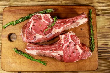 Kemiğin üzerinde çiğ biftek, baharatlar ve ahşap masada biberiye. Üst görünüm