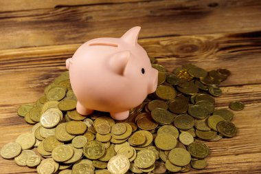 Ahşap arka planda bir yığın madeni paranın üzerindeki pembe kumbara. Para biriktirme kavramı