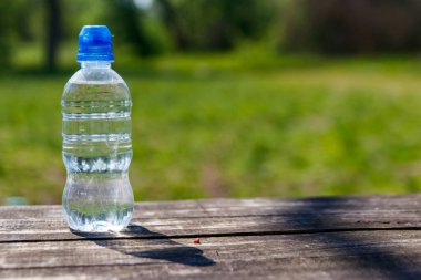 Doğanın arka planında, ahşap bir masanın üzerinde taze içme suyu olan plastik şişe.