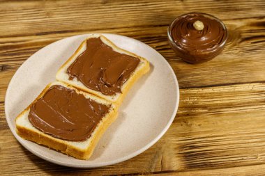 İki dilim ekmek ve ahşap masaya serilmiş fındıklı çikolata.