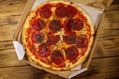 Tahta bir masanın üzerindeki karton kutuda nefis taze pizza. Üst Manzara. Yemek teslimatı, fast food, pizza teslimatı.