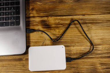 Harici HDD, tahta bir masadaki dizüstü bilgisayara bağlı. Üst Manzara. Veri depolama kavramı
