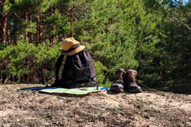 Yürüyüş botları, şapkası, pusulası ve haritası olan turist sırt çantası çam ormanında. Yürüyüş teçhizatı. Seyahat kavramı