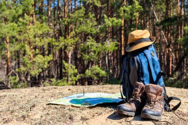 Yürüyüş botları, şapkası, pusulası ve haritası olan turist sırt çantası çam ormanında. Yürüyüş teçhizatı. Seyahat kavramı