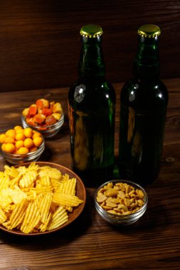 Bira şişeleri ve ahşap masada bira için çeşitli atıştırmalıklar.