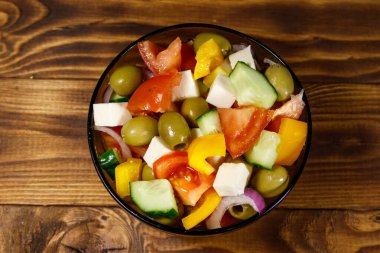 Taze sebze ile Yunan salatası, beyaz peynir ve yeşil zeytin cam ahşap masaya kase.