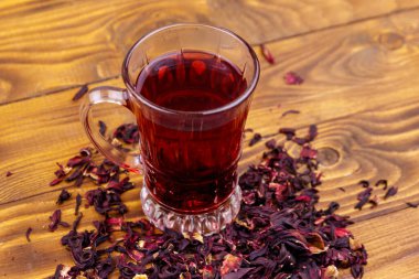 Ahşap masada bir bardak kırmızı amber çayı (carcade, roselle).
