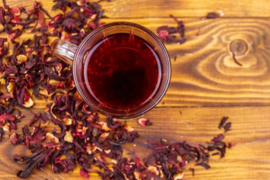 Ahşap masada bir bardak kırmızı amber çayı (carcade, roselle).