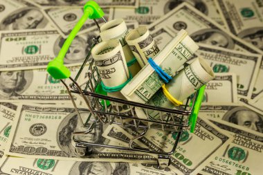 Amerika 'nın arka planında 100 dolarlık banknotlarla dolu küçük bir alışveriş arabası. Tüketici kavramı