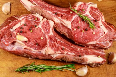 Baharat, sarımsak ve biberiye ahşap masada kemik çiğ taze sığır kaburga göz biftek. Üstte görüntü