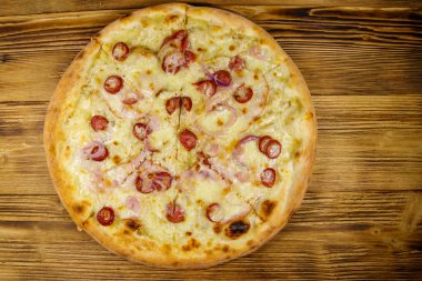 Ahşap bir masada sosisli, kırmızı soğanlı ve peynirli lezzetli taze pizza. Üst görünüm
