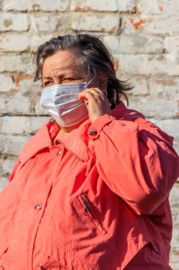 Kıdemli kadın yüzünde Coronavirus ve diğer virüs ve hastalıklara karşı koruyan tıbbi bir maske takıyor. Eski tuğla duvarın arka planında. Koronavirüs salgını